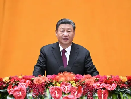Lider chinez susținând un discurs pe fond portocaliu, cu flori decorative.