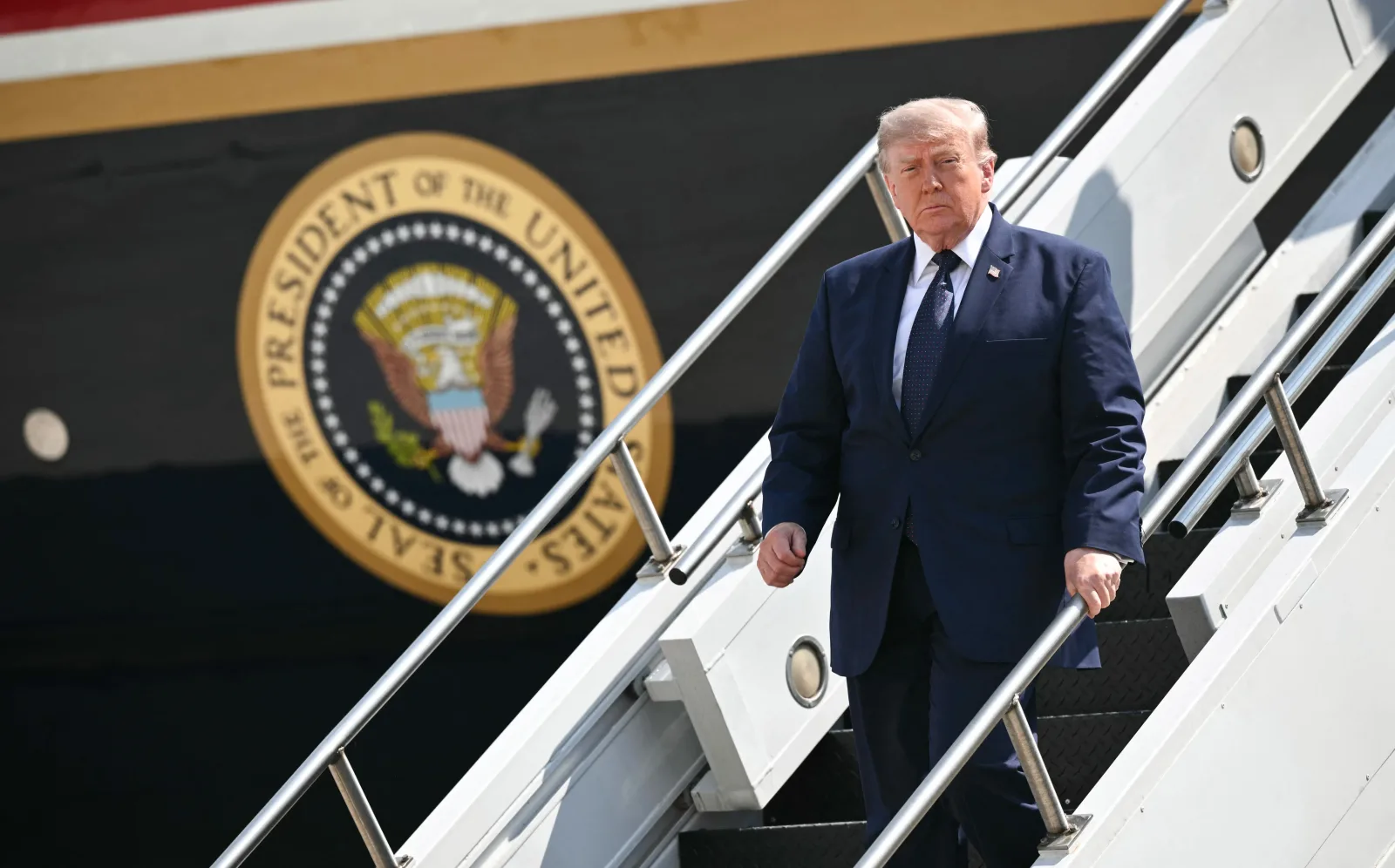 Donald Trump coboară de pe o scară, în fața unui avion prezidențial.
