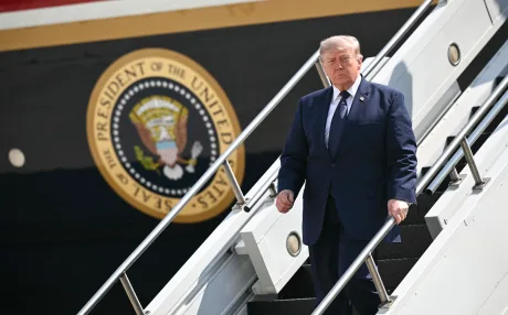 Donald Trump coboară de pe o scară, în fața unui avion prezidențial.