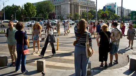 Oameni pe o stradă aglomerată, interacționând și traversând la semafor.