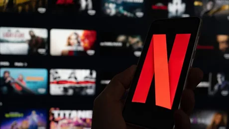 Logo-ul Netflix pe un telefon, cu fondul platformei de streaming.