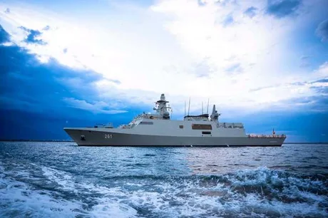 Nava militară navigând pe apă, sub un cer înnorat.