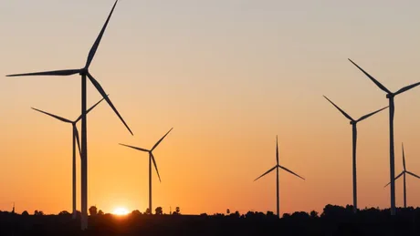 Turbine eoliene la apus, simbol al energiei regenerabile afectate de decizii guvernamentale.