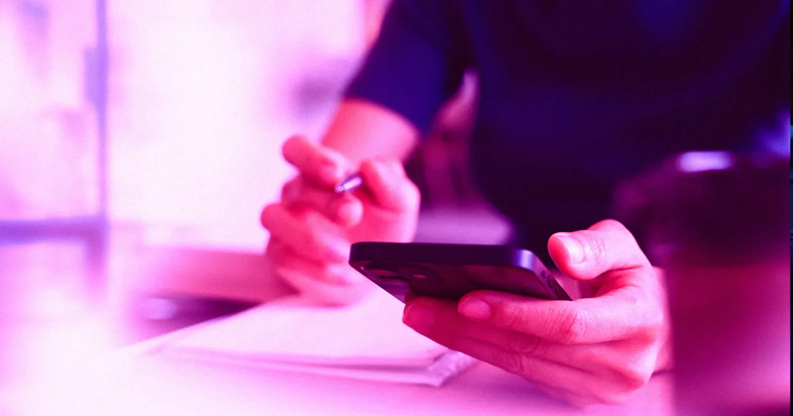 Utilizator tânăr interacționând cu un telefon mobil, scriind notițe.
