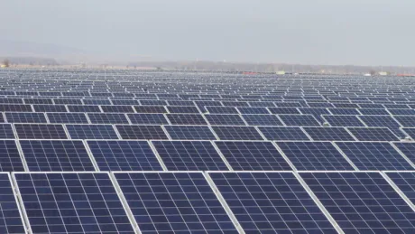 Panouri solare amplasate pe un teren vast, reflectând lumina soarelui.