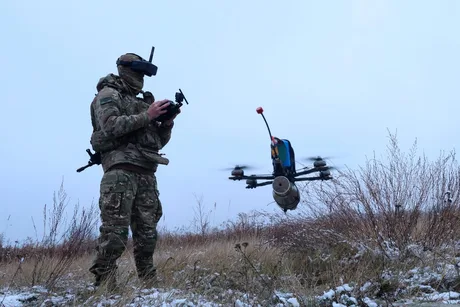 Soldat operând un drone într-un peisaj de iarnă, cu zăpadă pe pământ.