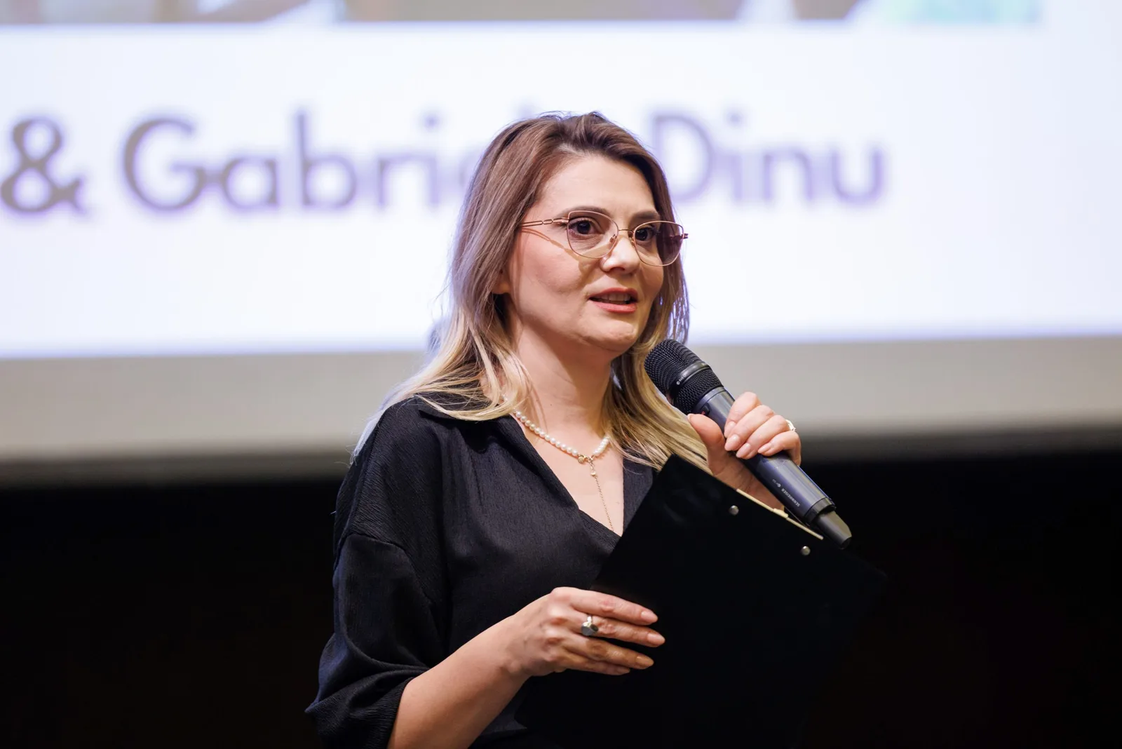 Prezentare a unei femei la un eveniment, vorbind la microfon.