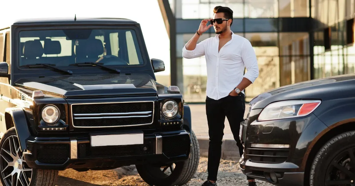 Bărbat lângă două autoturisme de lux într-un peisaj urban.