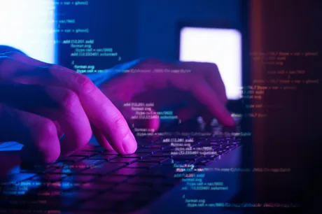 Mâini care tastează pe o tastatură, cu coduri de programare pe ecran.