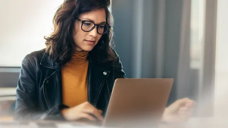 O femeie lucrează la laptop, concentrată pe sarcinile sale.