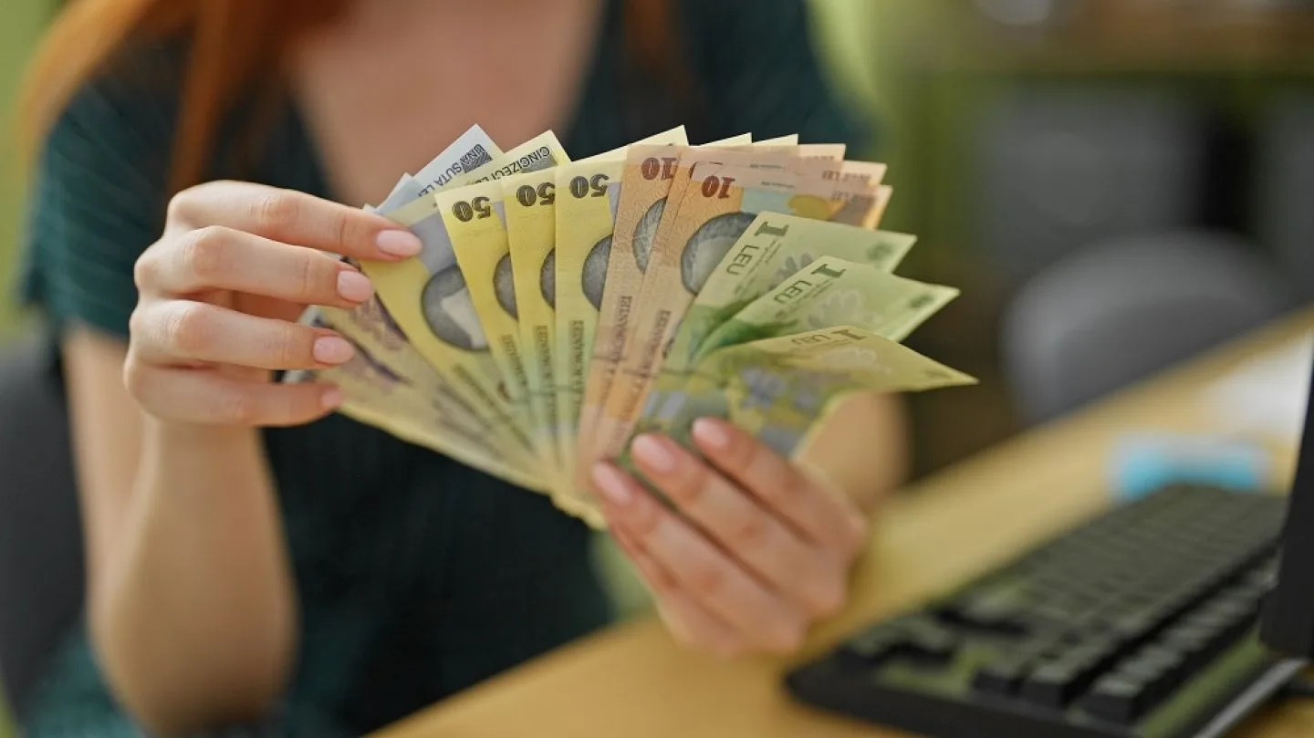 O persoană numără bancnote de lei pe un birou.