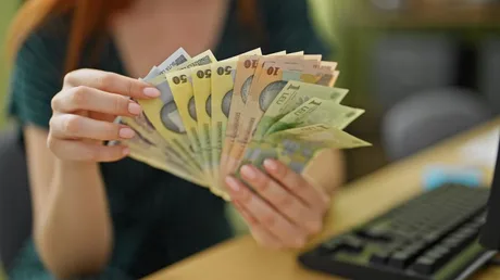 O persoană numără bancnote de lei pe un birou.
