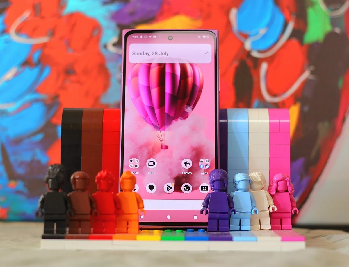Un telefon modern expus printre figurine colorate din plastic, cu un fundal artistic vibrant.