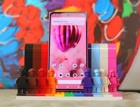 Un telefon modern expus printre figurine colorate din plastic, cu un fundal artistic vibrant.
