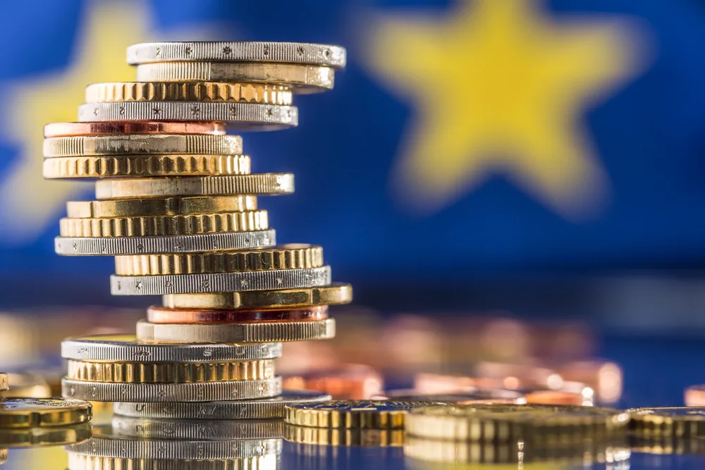 Monedele europene stivuite pe un fundal cu steagul Uniunii Europene.