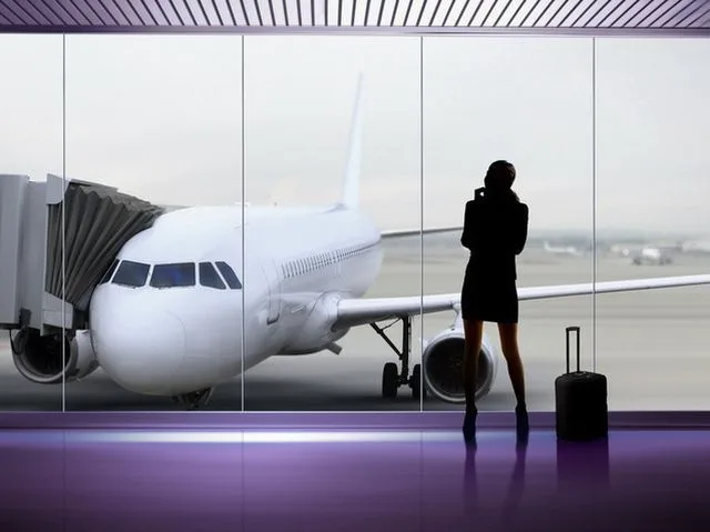 O pasageră așteaptă la aeroport, privind un avion pe pistă.