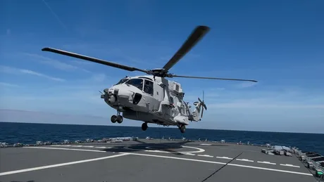 Elicopter Sea Tiger în acțiune, deasupra apei, cu un vas în fundal.