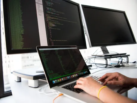 Un utilizator lucrează la un laptop cu două monitoare conectate.