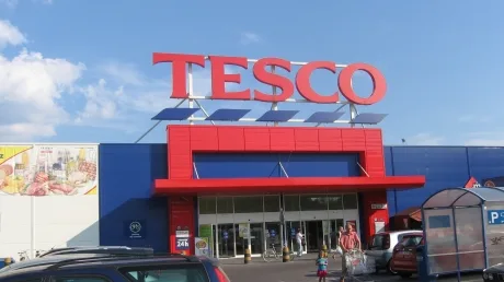 Intrarea unui magazin Tesco, cu semnul distinctiv și cer senin.