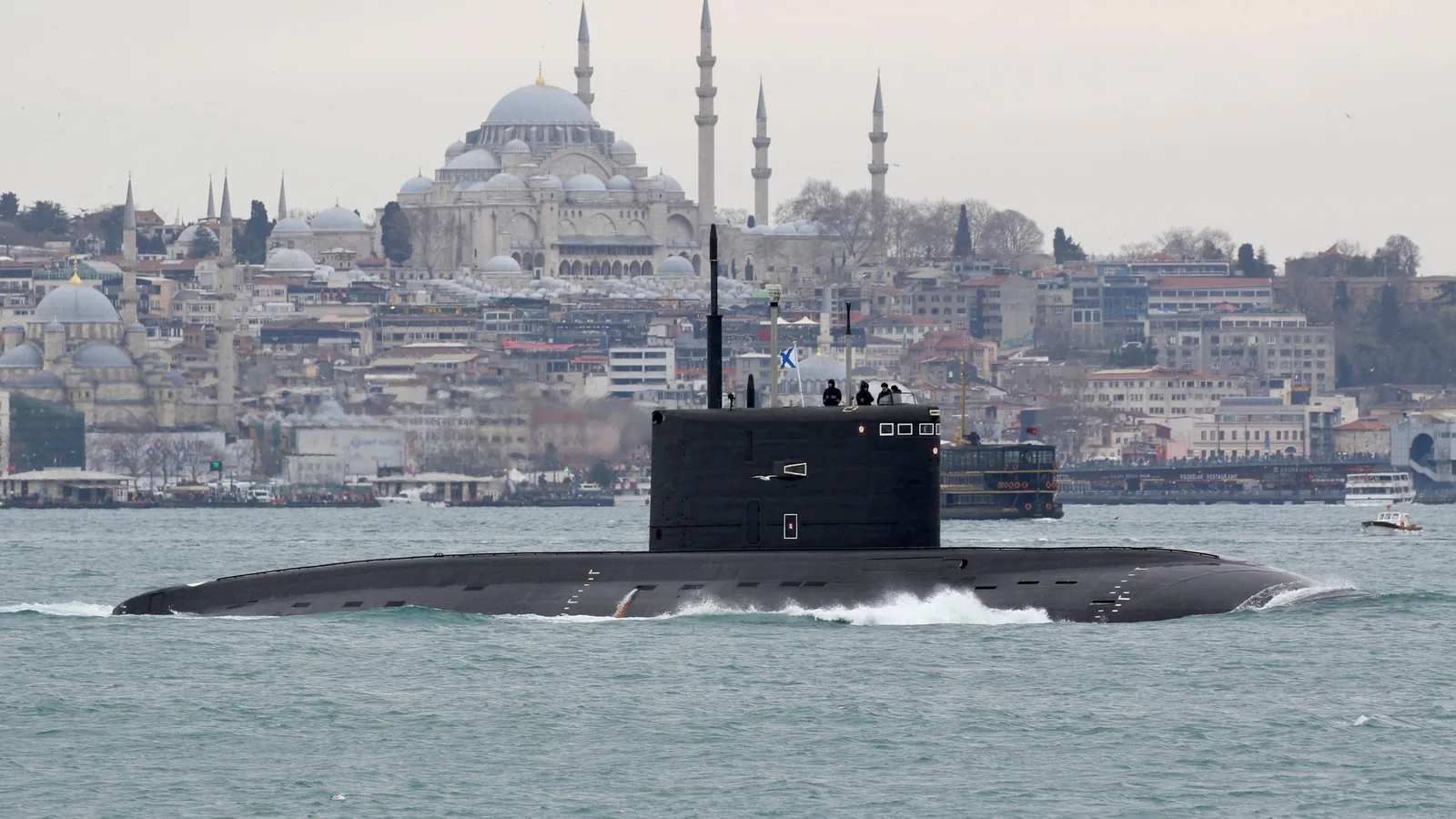 Submarin rusesc navigând pe Marea Neagră, cu orașul în fundal.