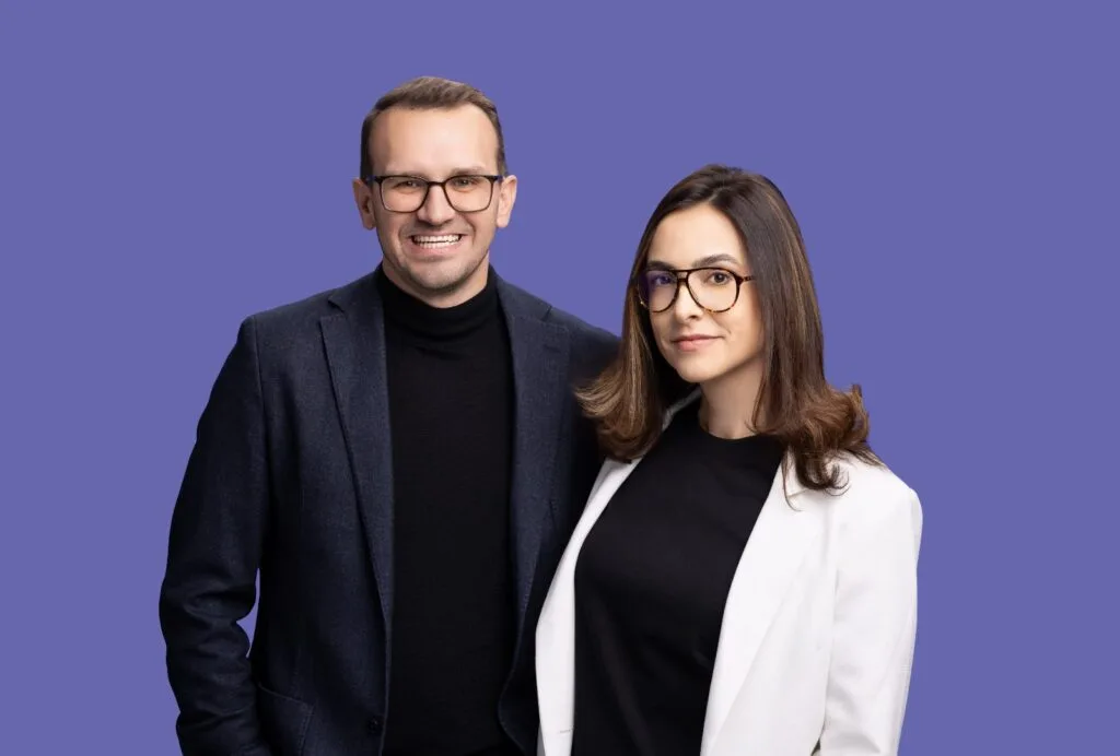 Doi profesioniști în marketing, zâmbind pe un fundal violet.