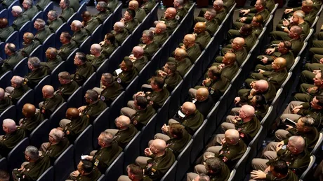 Militari așezați în rânduri, ascultând o prezentare oficială.