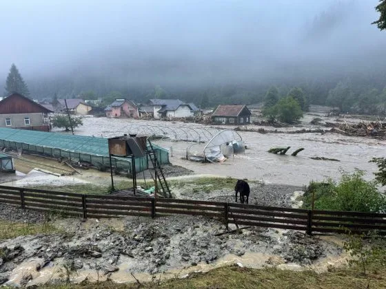 Peisaj afectat de inundații, case și terenuri inundate în zona rurală.