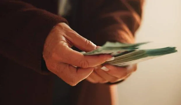 O mână numără bancnote, simbolizând probleme financiare și fraude fiscale.