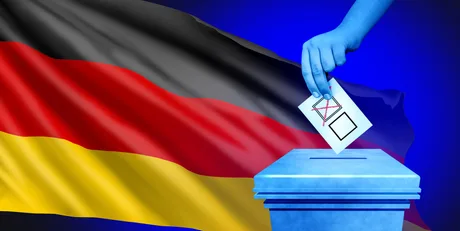 O mână introduce un buletin de vot într-o urnă, cu steagul Germaniei în fundal.