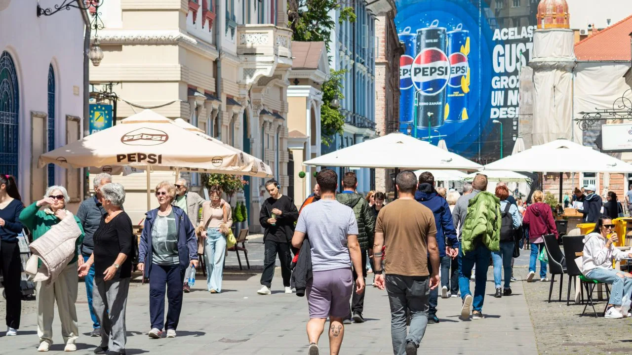 Oameni pe o stradă aglomerată, bucurându-se de vremea frumoasă.