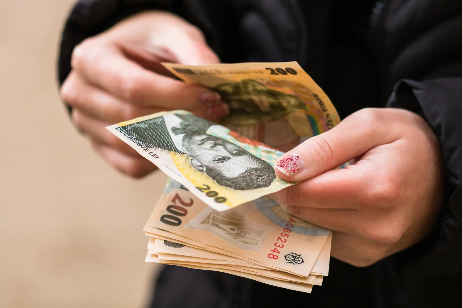 O persoană numără bancnote românești de diverse valori.