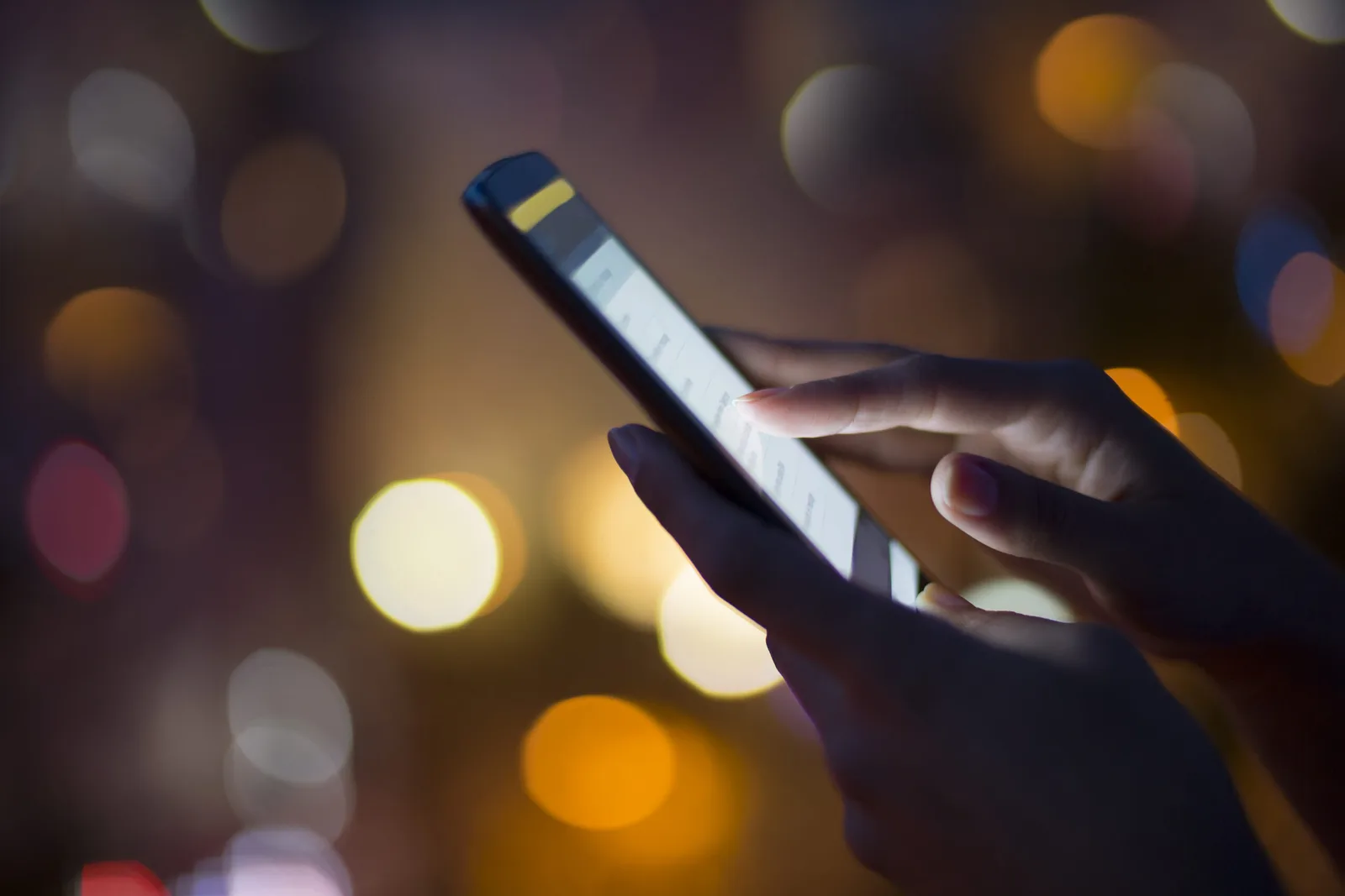 Utilizator interacționând cu un smartphone în lumina nocturnă.
