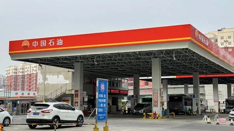 Stație de benzină din China, cu vehicule parcate și clădiri în fundal.
