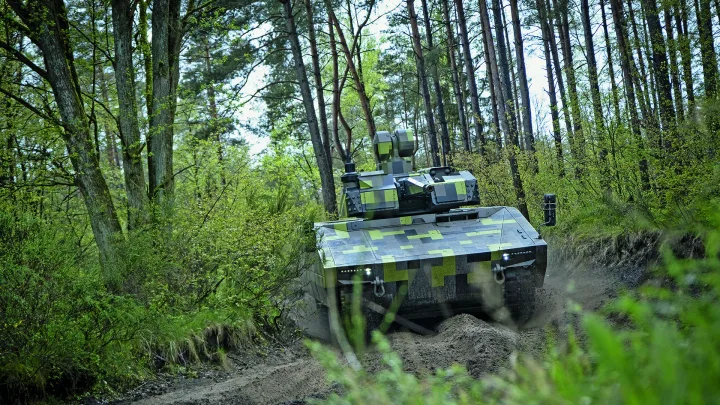 Tanc militar avansat pe un drum forestier, înconjurat de copaci verzi.