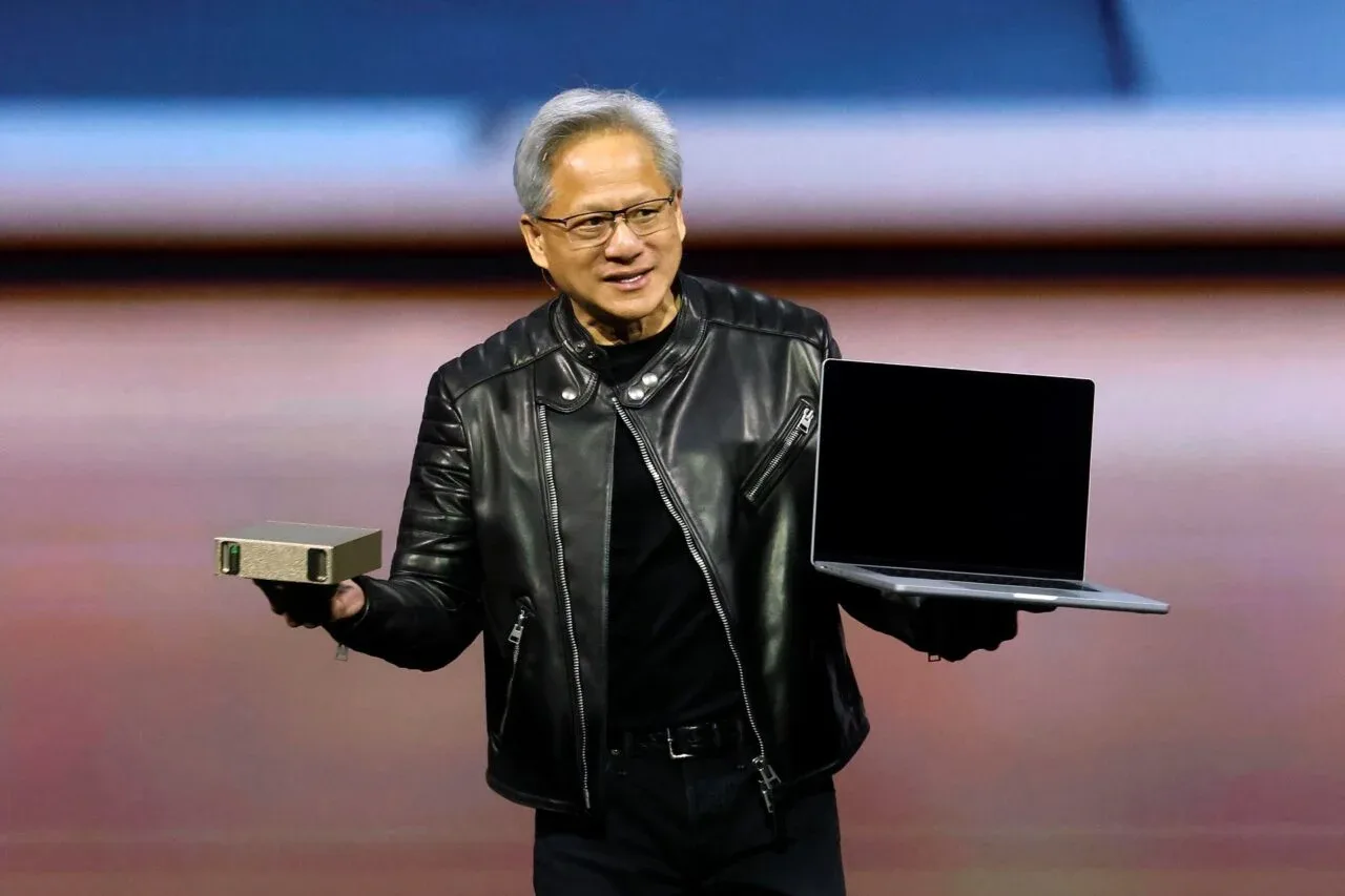 Jensen Huang prezentând un laptop și un dispozitiv, purtând o geacă de piele.