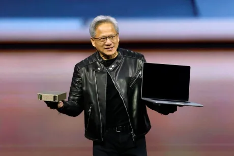 Jensen Huang prezentând un laptop și un dispozitiv, purtând o geacă de piele.
