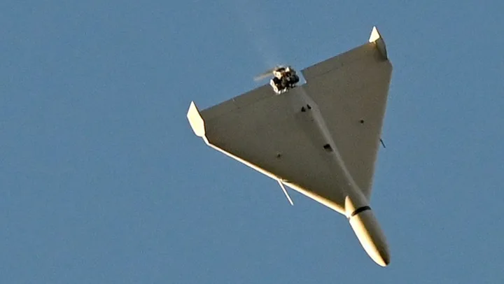 Dronă de tip militar zburând pe un fundal albastru, însoțită de nori pufoși.