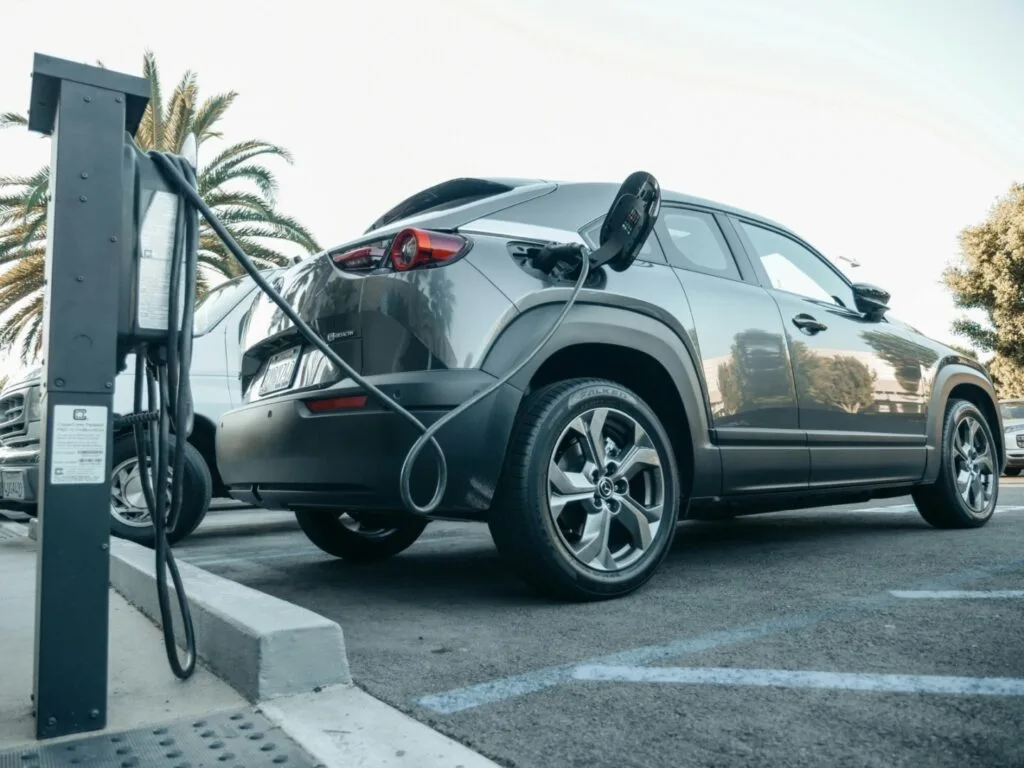 Mașină electrică conectată la o stație de încărcare într-o parcare.