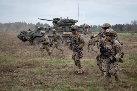 Soldați americani în exercițiu militar pe teren deschis, cu un tanc în fundal.