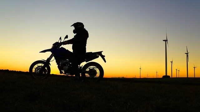 Motociclist pe fundalul unui apus, cu turbine eoliene în depărtare.