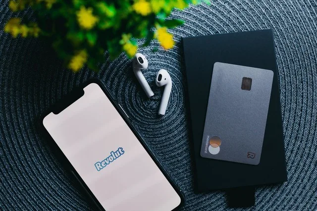 Un telefon mobil cu aplicația Revolut și o carte de credit pe un fundal texturat.