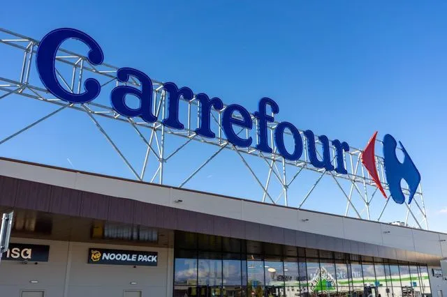 Logo-ul Carrefour pe fațada unui magazin modern, sub un cer senin.