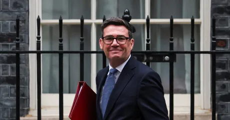 Andy Burnham zâmbind în fața unei clădiri guvernamentale din Londra.