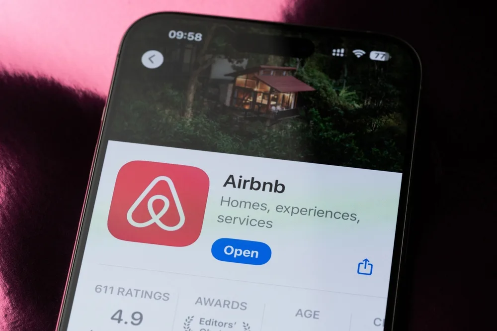 Aplicația Airbnb pe un telefon mobil, cu fundal verde și detalii despre anunțuri.
