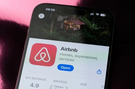 Aplicația Airbnb pe un telefon mobil, cu fundal verde și detalii despre anunțuri.
