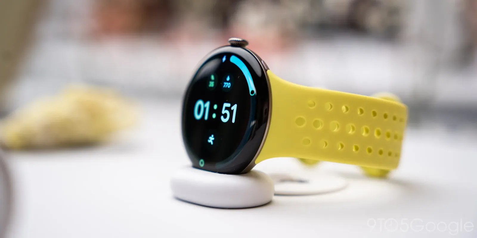 Pixel Watch 5 cu curea galbenă, pe suport de încărcare.