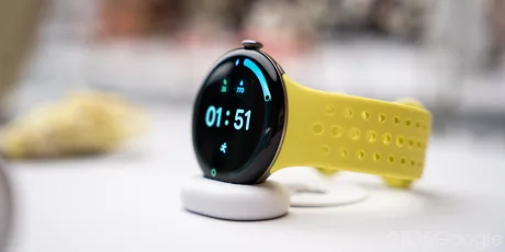 Pixel Watch 5 cu curea galbenă, pe suport de încărcare.