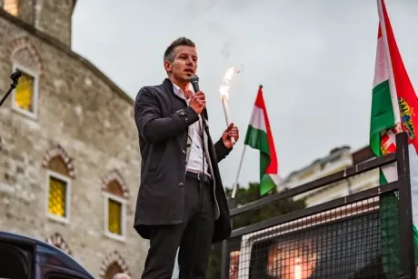 Un politician vorbește la un miting, cu steaguri ungurești în fundal.