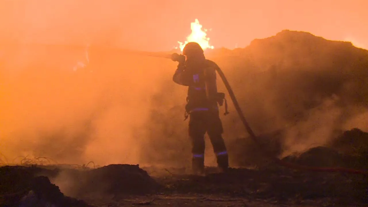Pompier stingând flăcările unui incendiu la un depozit de reciclare.