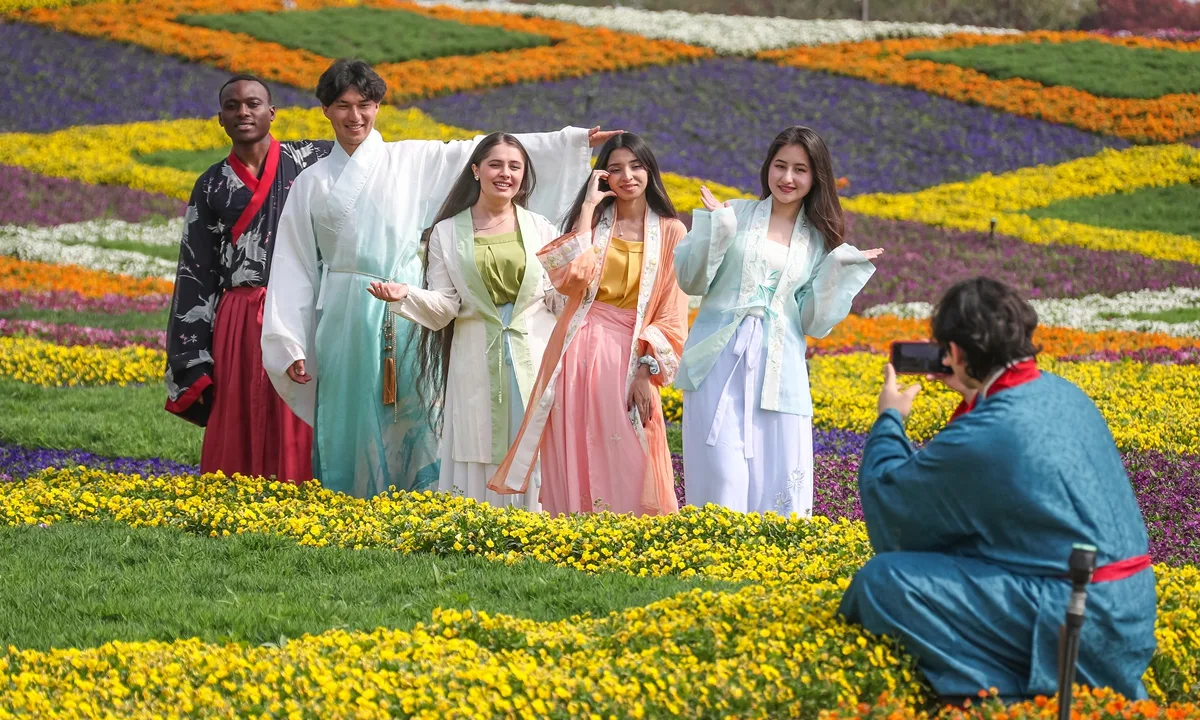Tineri îmbrăcați în costume tradiționale, pozând într-un câmp plin de flori.